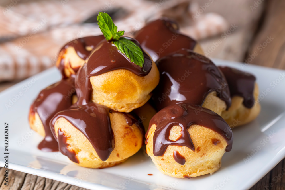 Delicious profiteroles with chocolate and white plate. Selective focus image on light background.