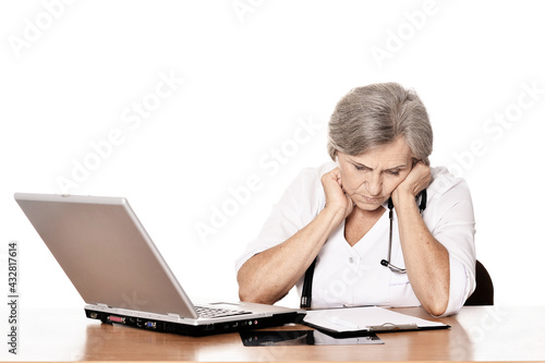 Serious elderly woman doctor sitting at table with computer Serious elderly woman doctor sitting at table with computer