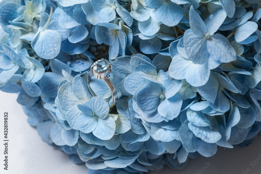 Fashion silver or white gold ring with a blue rectangular aquamarine stone. Elegant topaz ring for women. Jewelry ring with a precious stone. Blue flowers background.