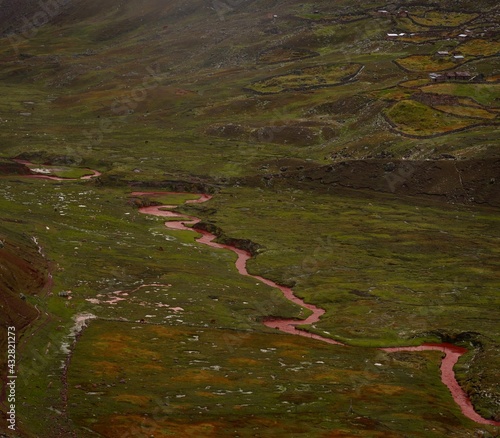 Red sandstone mineral sediment coloured river stream in green grass valley at Vinicunca Rainbow Mountain in Cusco Peru photo