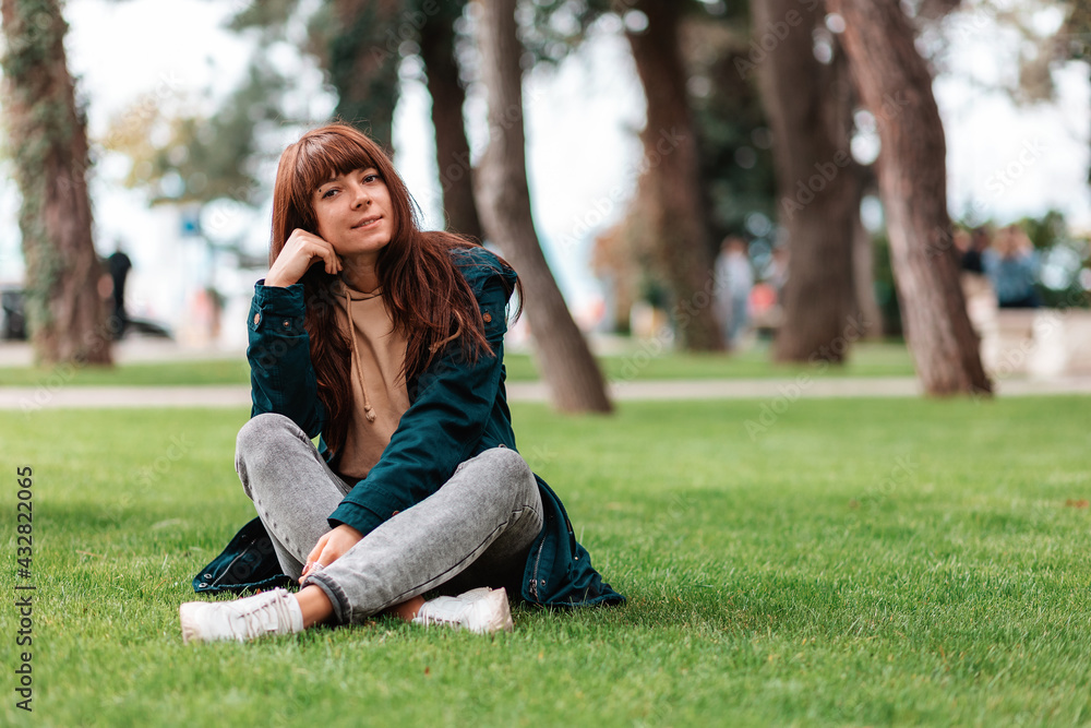 A young smiling woman sits cross-legged on the grass. Recreation in the park. Copy space A young smiling woman sits cross-legged on the grass. Recreation in the park. Copy space