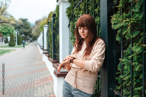 A young pretty woman looks at her wristwatch. Outdoor. The concept of waiting
