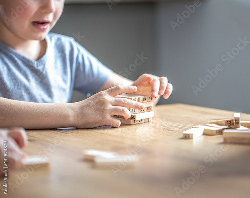 Little boy stands a turret with wooden cubes close up.