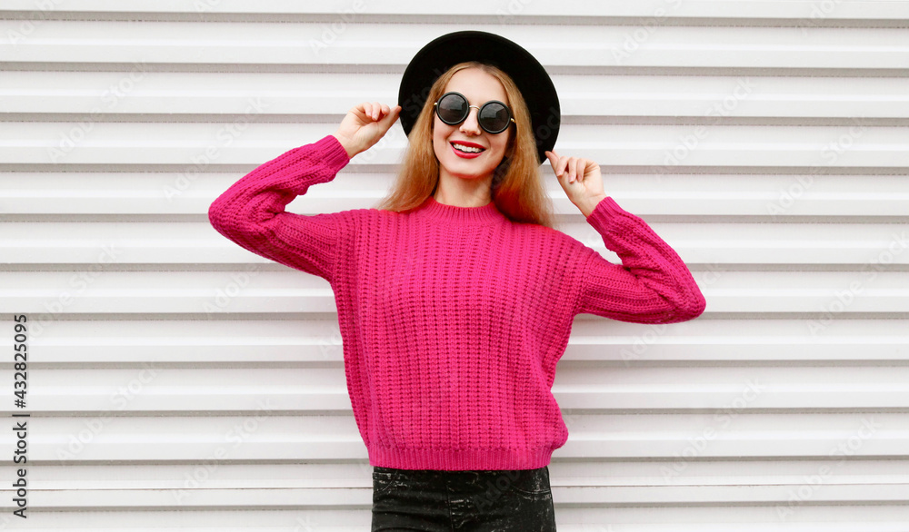 Portrait of happy smiling young woman model wearing a pink knitted sweater and black round hat on a white background
