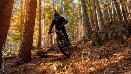 Obraz na płótnie A man on a bicycle through the forest from a mountain on a bright sunny day. The guy rides through the trees. Cyclists riding a mountain electric bicycle steep uphill in harsh rocky terrain w salonie