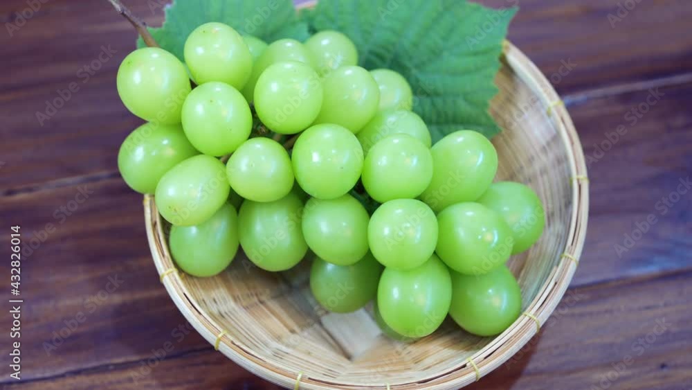 Green grape in Bamboo basket on wooden table in garden, Japanese Shine Muscat Grape with leaves in wooden background Green grape in Bamboo basket on wooden table in garden, Japanese Shine Muscat Grape with leaves in wooden background