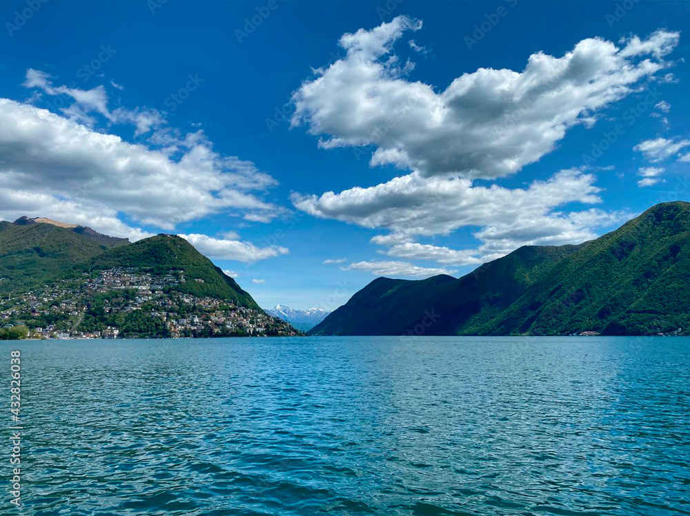 Lake Lugano. Switzerland. City center, embankment. View of the lake and mountains. Sunny day, clouds. Wallpaper