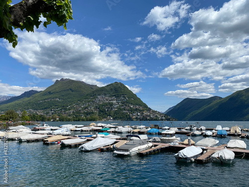 Lake Lugano. Switzerland. City center, embankment. View of the lake and mountains. Parked boats near the shore. Sunny day, clouds. Wallpaper