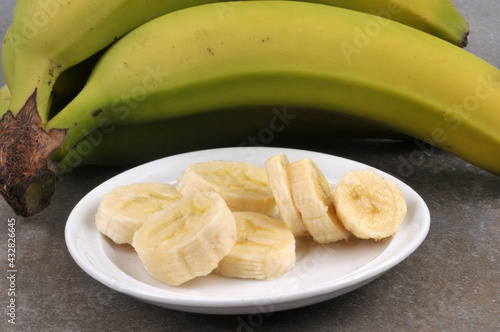 Banane coupée en rondelles dans une soucoupe en gros plan avec des bananes au second plan photo