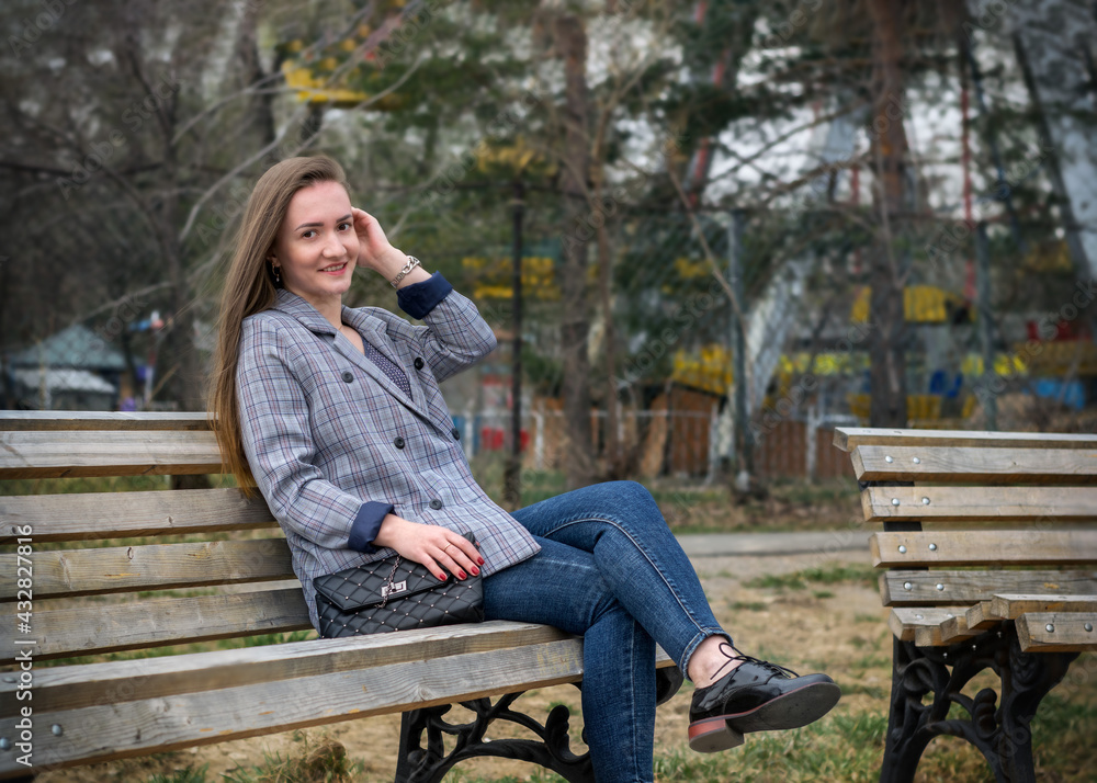 A young, pretty girl is sitting on a bench in a sunny afternoon park. A young, pretty girl is sitting on a bench in a sunny afternoon park.