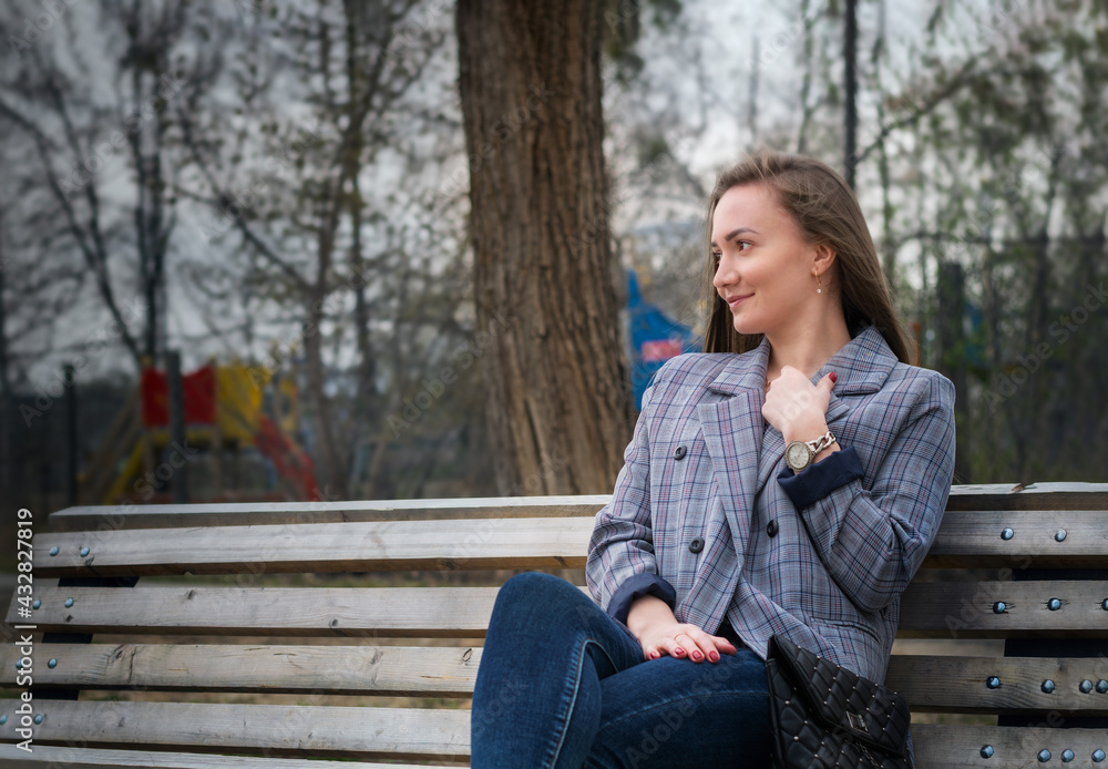 A young, pretty girl is sitting on a bench in a sunny afternoon park. A young, pretty girl is sitting on a bench in a sunny afternoon park.