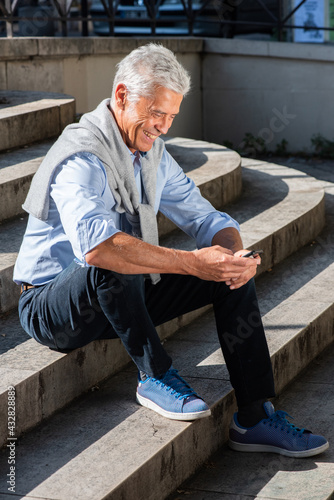Full body alderman sitting outside using mobile phone
