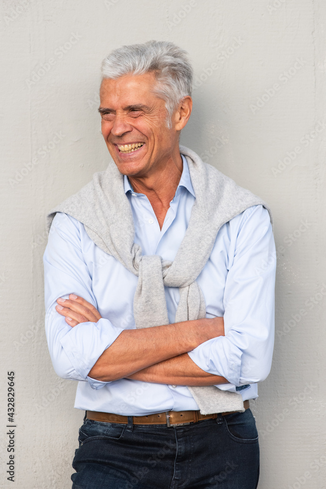 smiling older man with arms crossed by white wall looking away smiling older man with arms crossed by white wall looking away