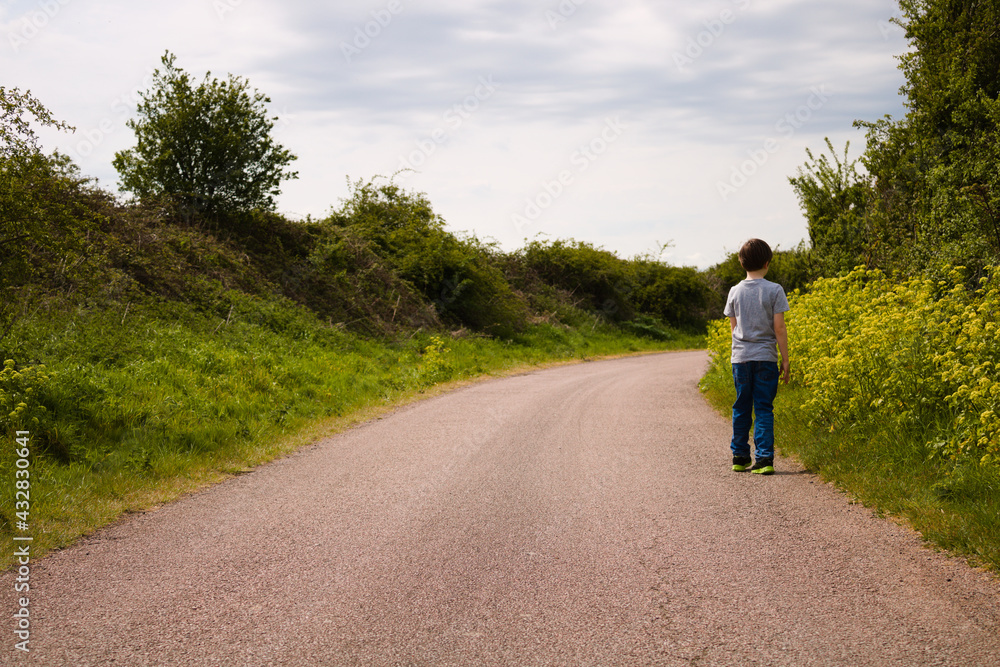 Boy walking up the rural empty road with foliage on the sides, dramatic sky landscape