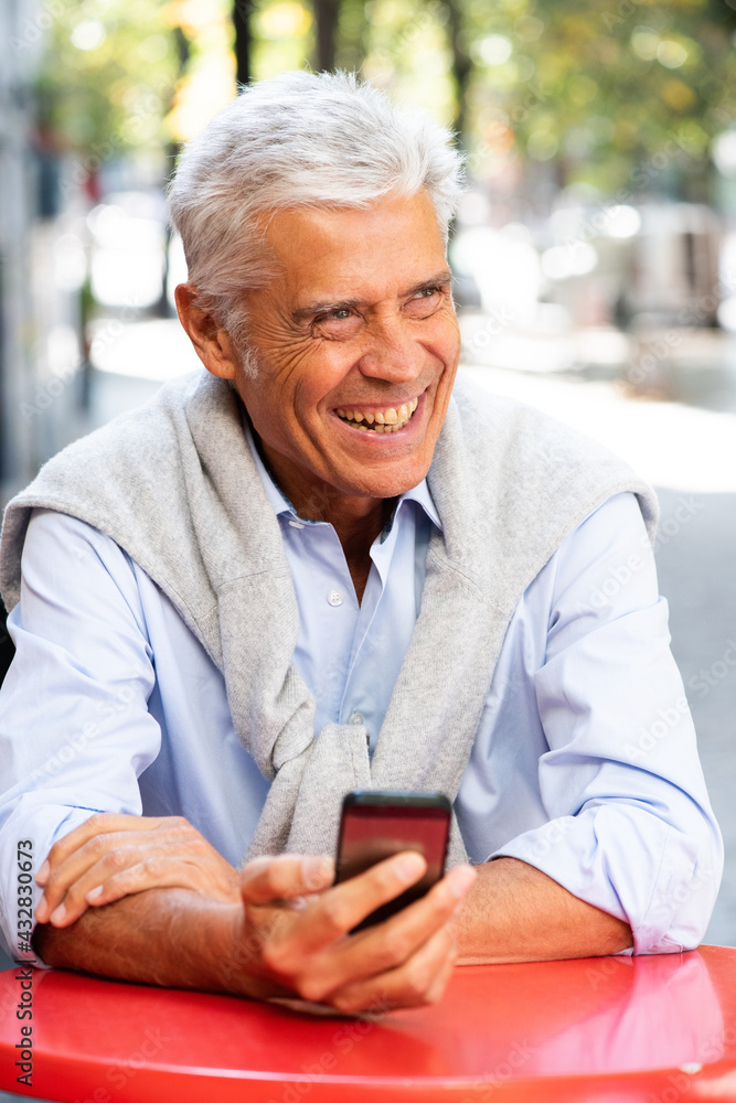 Obraz premium Close up smiling older man sitting at table with cellphone in hand