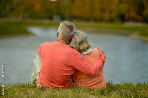 Happy senior woman and man in park sitting by pond