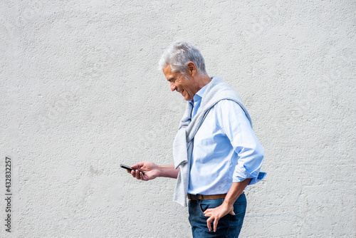 Profile of older man holding mobile phone against white wall