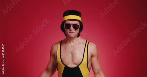 Funny retro athlete man in yellow tracksuit and sunglasses from 80's s makes the workout jumps isolated on red background. Retro sport hipster show off and posing in front of camera. photo