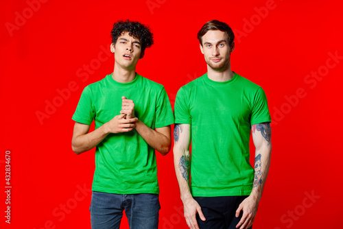 Two cheerful friends in green t-shirts joy of communication red background