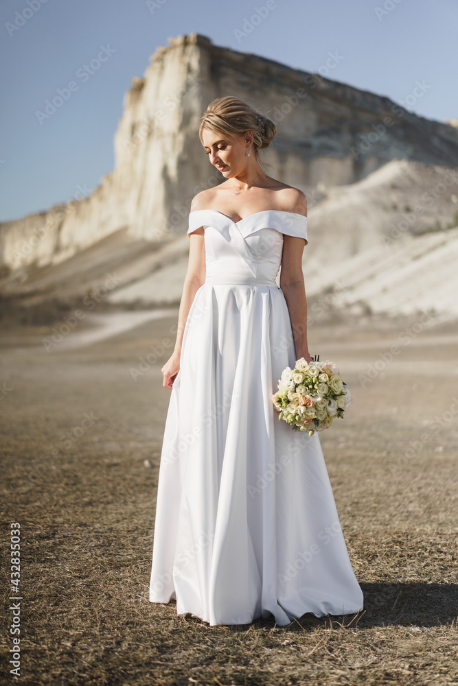 Beautiful bride in a wedding dress with a bouquet standing against white rock