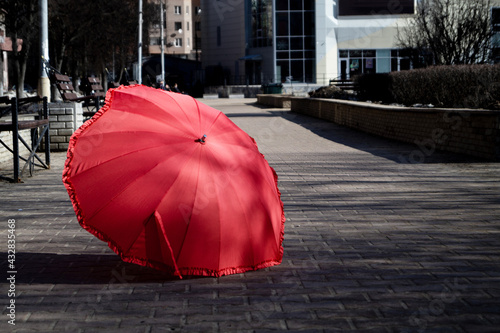 Fototapeta Naklejka Na Ścianę i Meble -  a red umbrella lies outside on a stone sidewalk on a spring autumn summer sunny day