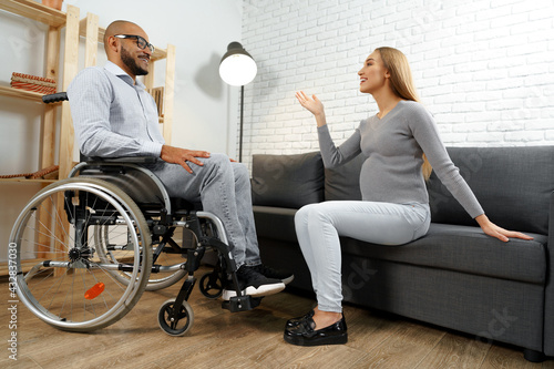 Disabled african american man in wheelchair talking to his pregnant wife in the living room photo