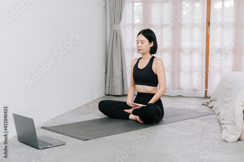 Asian young sporty slim woman coach internet video online training oga instructor modern laptop screen meditate relax breathe easy seat pose gym healthy lifestyle concept.