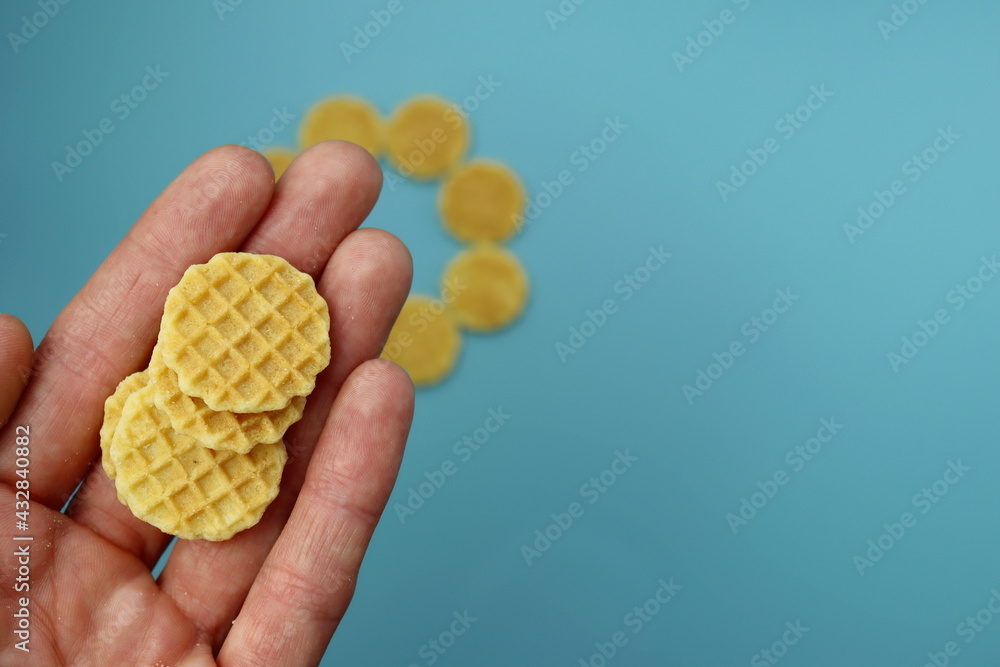 Small round waffles in a female hand on a blue background. Small round waffles in a female hand on a blue background.