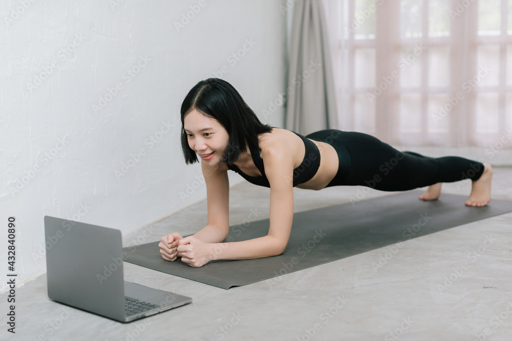 Girl training at home, exercising and watching videos on laptop, training in living room Girl training at home, exercising and watching videos on laptop, training in living room
