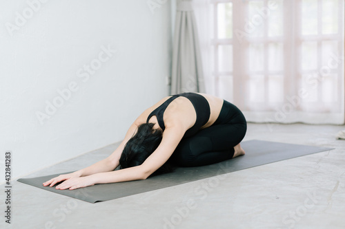 Young healthy beautiful asian woman in sportive top and leggings practicing yoga at home sitting on yoga mat relaxed, yoga concept