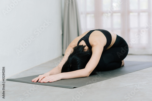 Young healthy beautiful asian woman in sportive top and leggings practicing yoga at home sitting on yoga mat relaxed, yoga concept