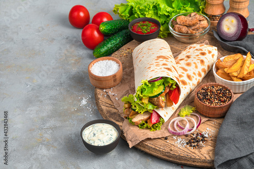 Shawarma with turkey, French fries and fresh vegetables on a gray background.