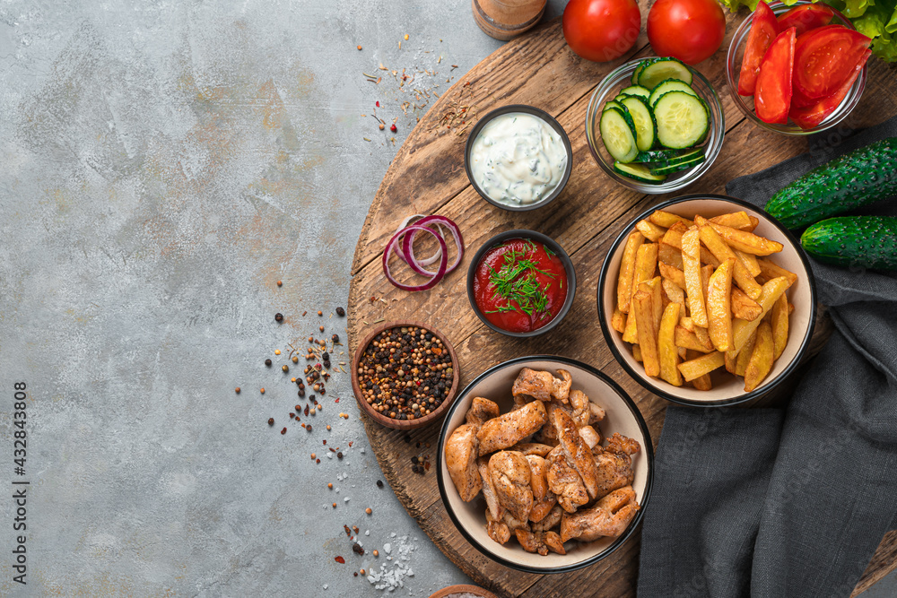 Fried potatoes, chicken meat and vegetables on a wooden board on a gray background. Fried potatoes, chicken meat and vegetables on a wooden board on a gray background.