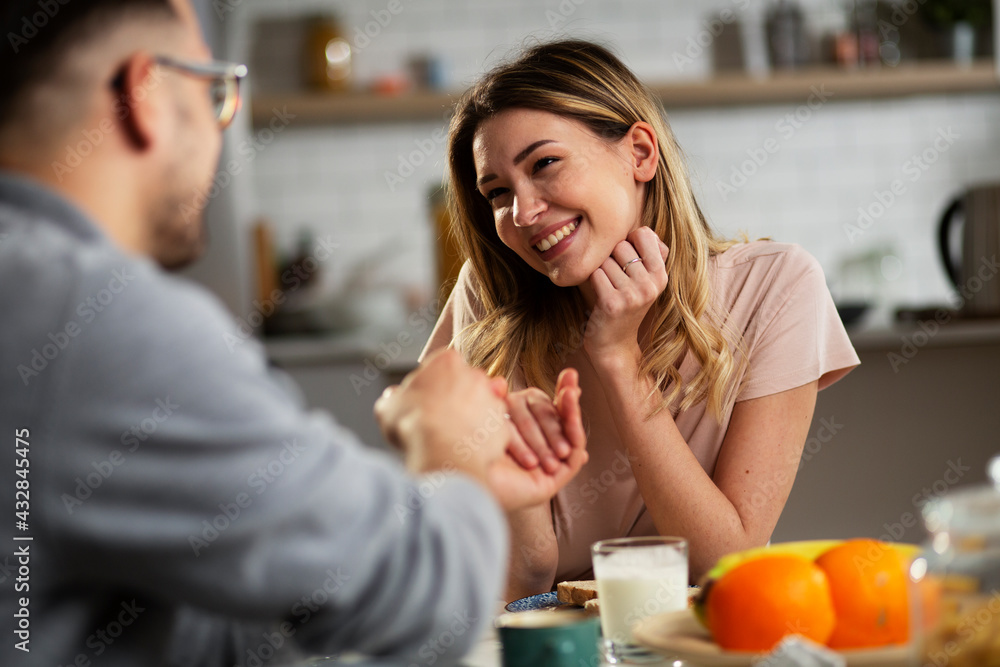 Beautiful young girl enjoying in breakfast with her boyfriend. Loving couple drinking coffee in the kitchen..