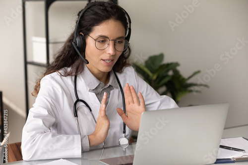 First aid online. Confident female therapist gp wear headphones consult patient by video call explain treatment give recommendations. Young woman doctor help sick person remotely using conference app