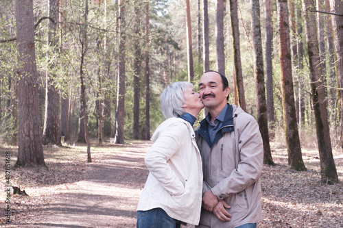 Elderly interracial couple in a spring forest park. A woman kissing a man on the cheek.