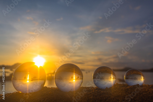 .The 4 glass balls are arranged from large to small placed on the beach at sunrise. .To see the sea upside down in a glass ball. A image for a unique and creative travel idea...