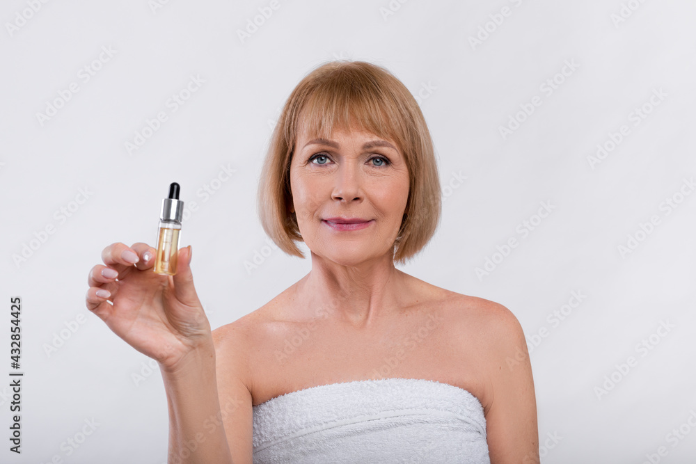 Beauty routine procedures. Sensual mature woman showing bottle with anti-aging serum on light studio background Beauty routine procedures. Sensual mature woman showing bottle with anti-aging serum on light studio background