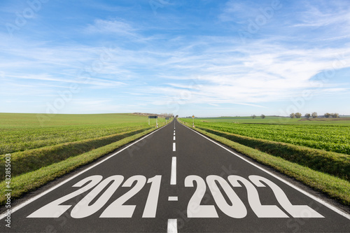 Empty road surrounded by green fields and the years 2021-2022 written 