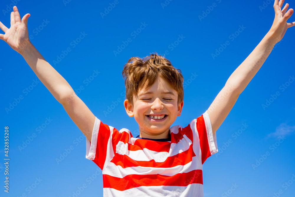 Happy boy raising hands over blue sky. Feel freedom , enjoying life and nature. Summer holidays concept Happy boy raising hands over blue sky. Feel freedom , enjoying life and nature. Summer holidays concept