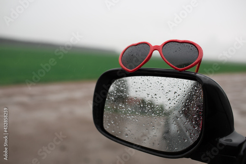 Car mirror in raindrops and red heart shaped sunglasses 