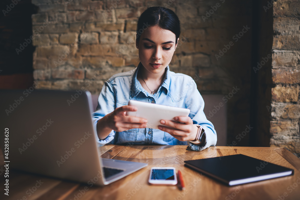 Wistful woman typing on tablet in light workspace Wistful woman typing on tablet in light workspace