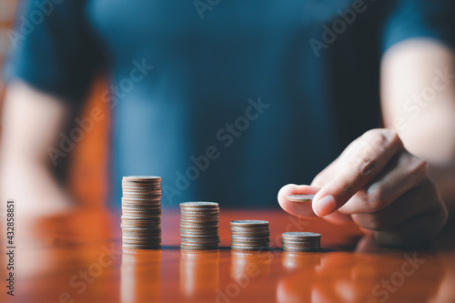 Closeup man hands. Businessman holding coin to place on stack of coins placed on the table. Accounting, Financial investment, saving money for future growth concept