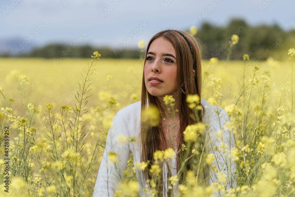 young woman sitting and pensive in a field of yellow flowers young woman sitting and pensive in a field of yellow flowers