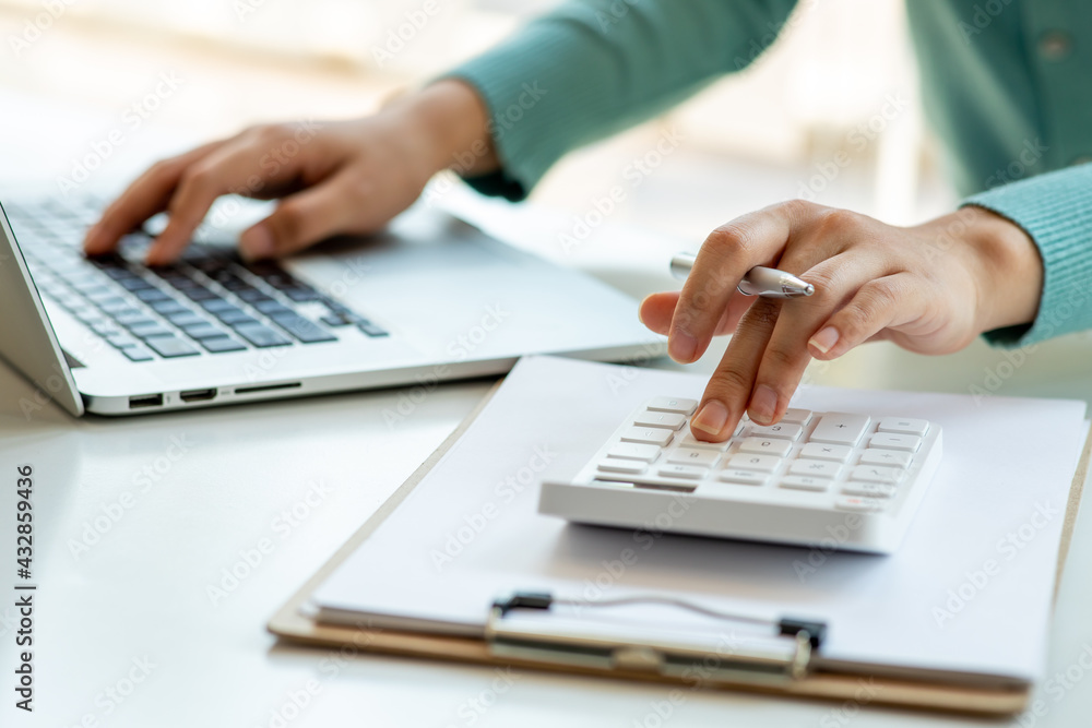 Close up Business woman using calculator and laptop for do math finance on wooden desk, tax, accounting, statistics and analytical research concept Close up Business woman using calculator and laptop for do math finance on wooden desk, tax, accounting, statistics and analytical research concept