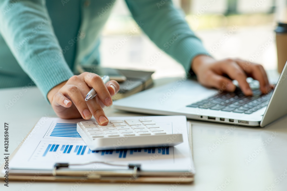 Close up Business woman using calculator and laptop for do math finance on wooden desk, tax, accounting, statistics and analytical research concept Close up Business woman using calculator and laptop for do math finance on wooden desk, tax, accounting, statistics and analytical research concept