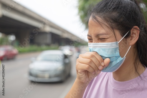 A woman wearing a mask is waiting for a car.