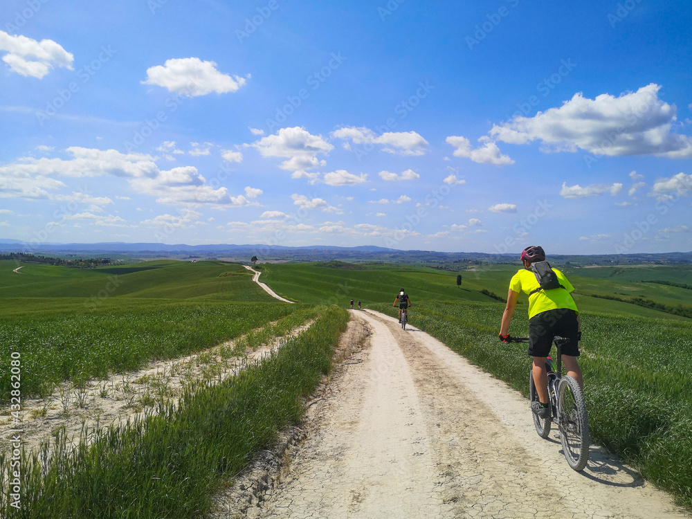 Fototapeta premium Ragazzo fa escursione in bicicletta sul sentiero tra i campi di grano in collina in toscana