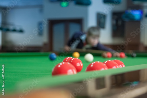 Teenager is playing snooker. Red balls are in the foreground.
