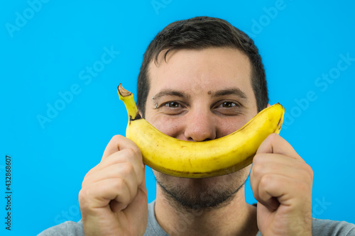 Giovane ragazzo si diverte creando un sorriso con una banana su sfondo blu